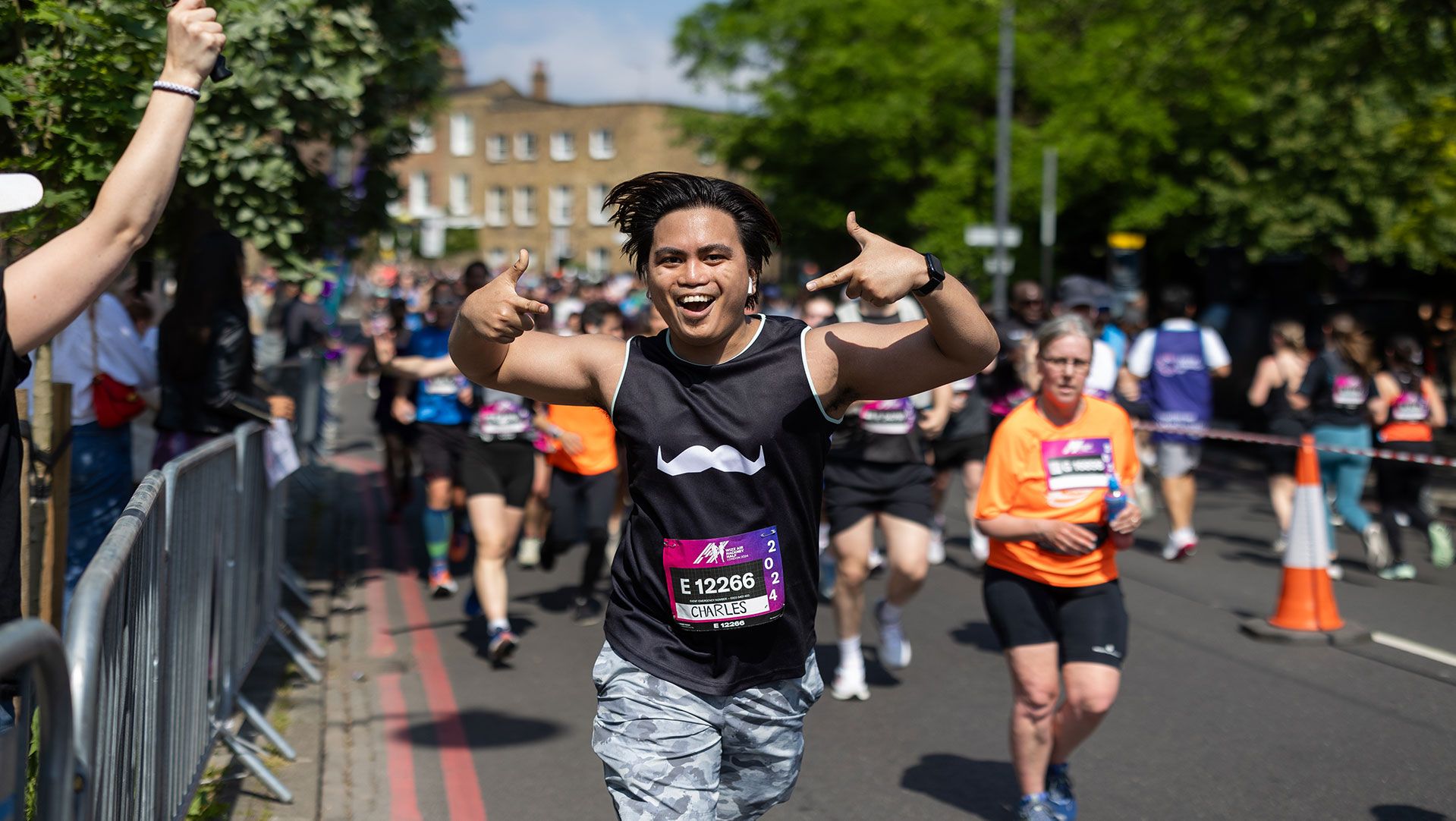 Photo of an athletic young man running in a marathon, enthusiastically gesturing to the camera.