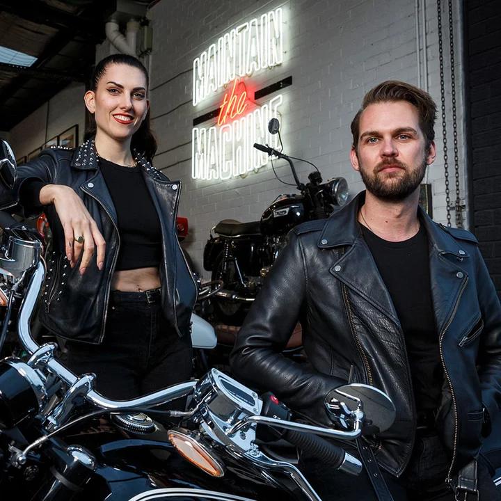 Two motorcyclists in leathers posing in front of motorcycles.