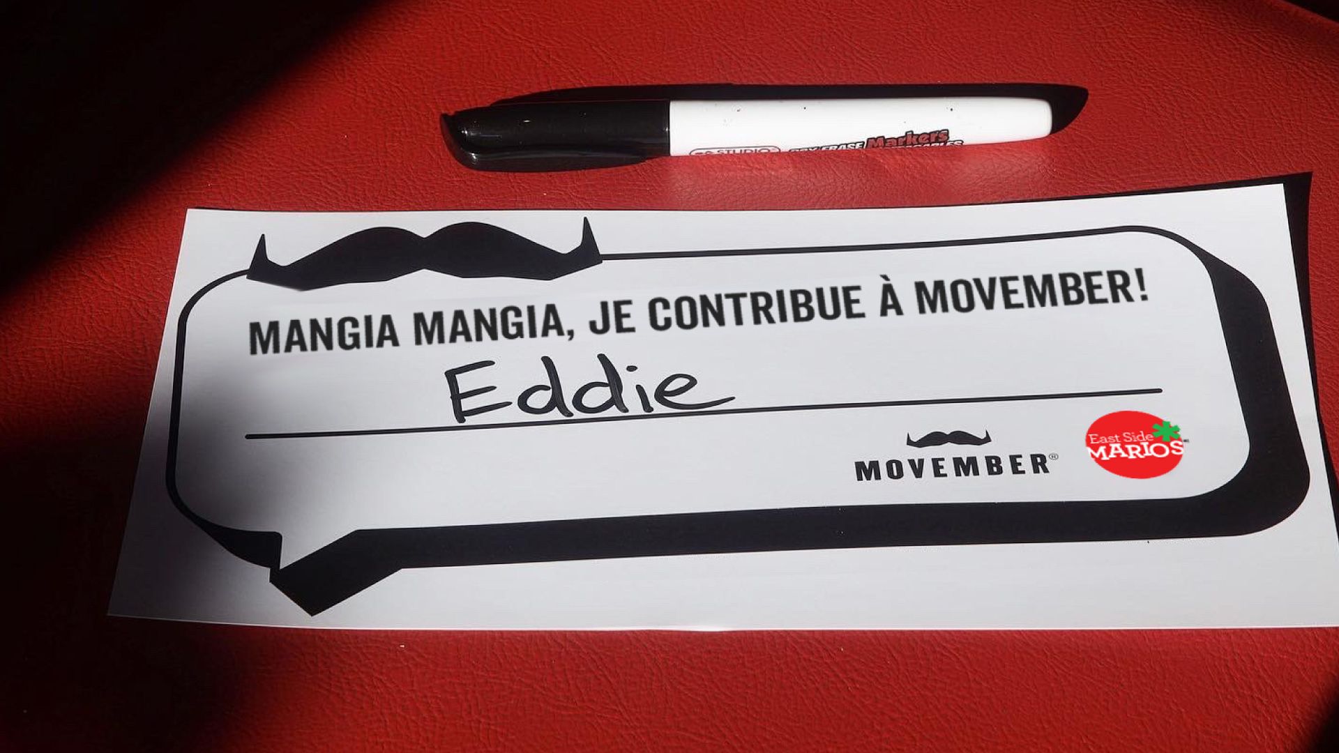 "I mangia mangiaed for Movember" apparaît sur un morceau de papier posé sur une chaise rouge de restaurant.