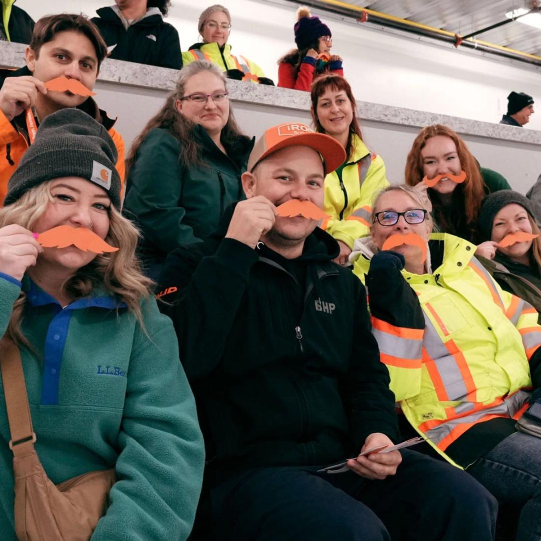 Photo of BHP staff, holding orange Movember cut-out moustaches to camera.