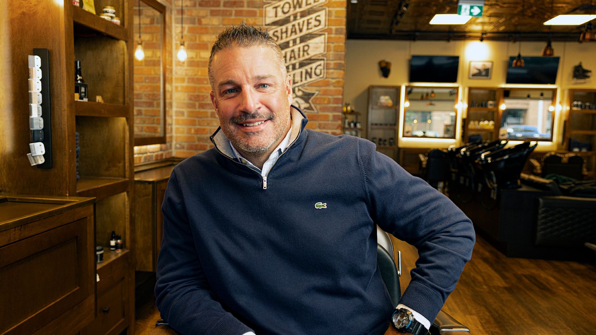Movember supporter Greg Filipchuk from SECURE, seated in a barber shop and smiling to camera.