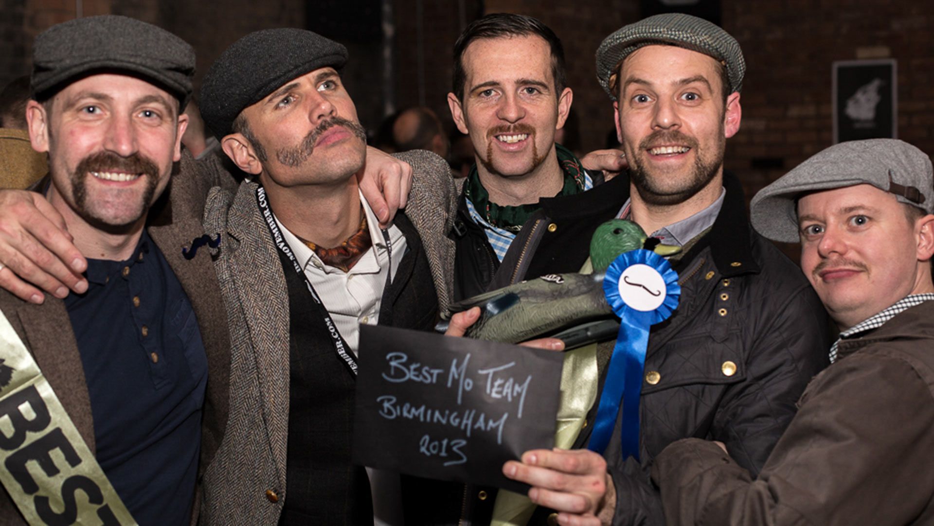 Photo showing five smiling men with magnificent moustaches, winning a Movember award.
