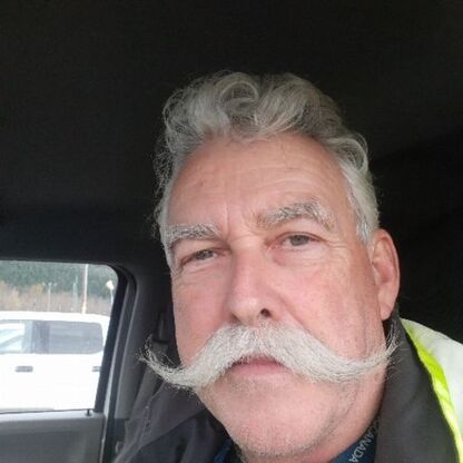 Man with large, glorious, grey moustache, looking to camera from within a motor vehicle.