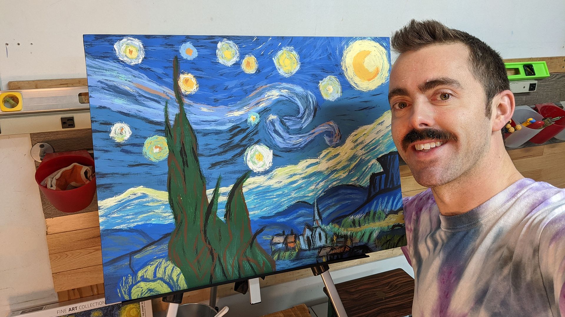 A moustachioed man poses with Van Gogh's Starry Night painting (a swirl of blue and yellow) -- a painting that he painted with his moustache as the brush