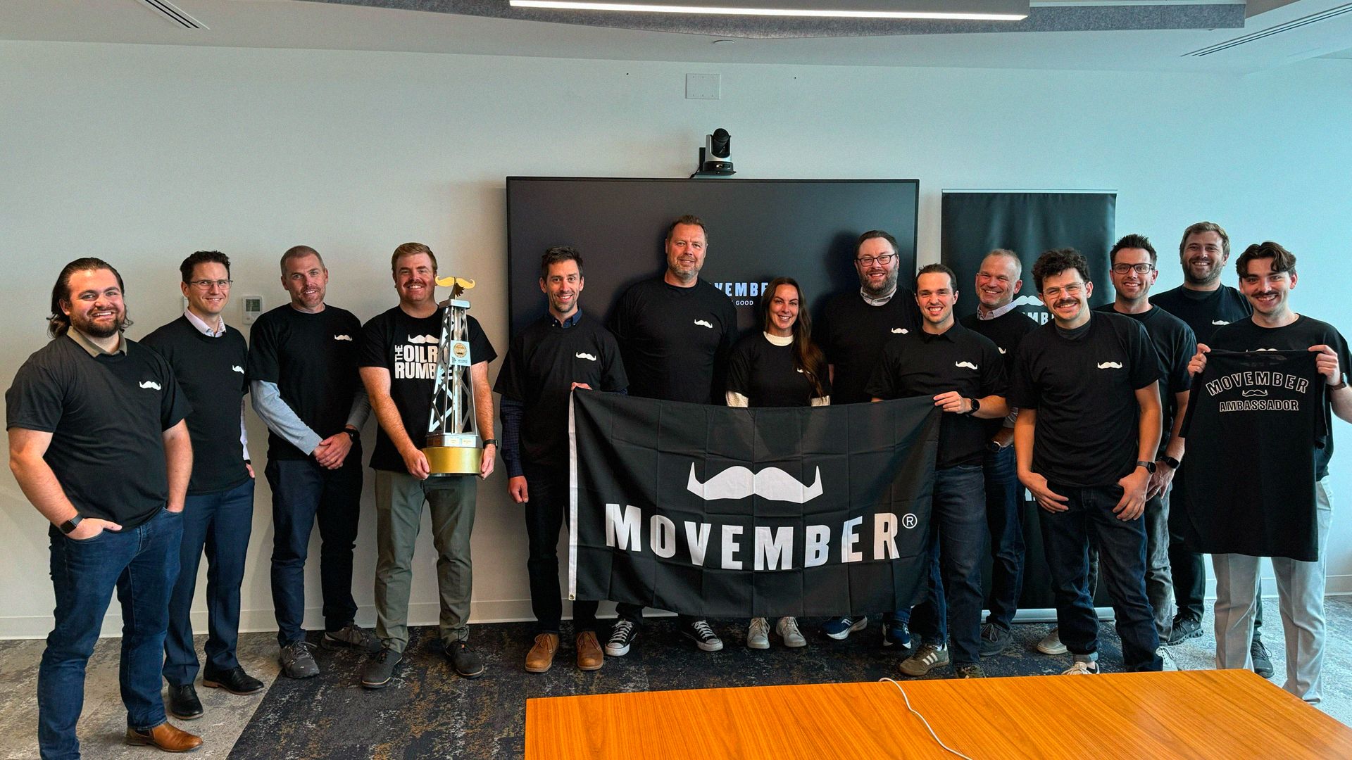 Group of colleagues post with a Movember flag at work