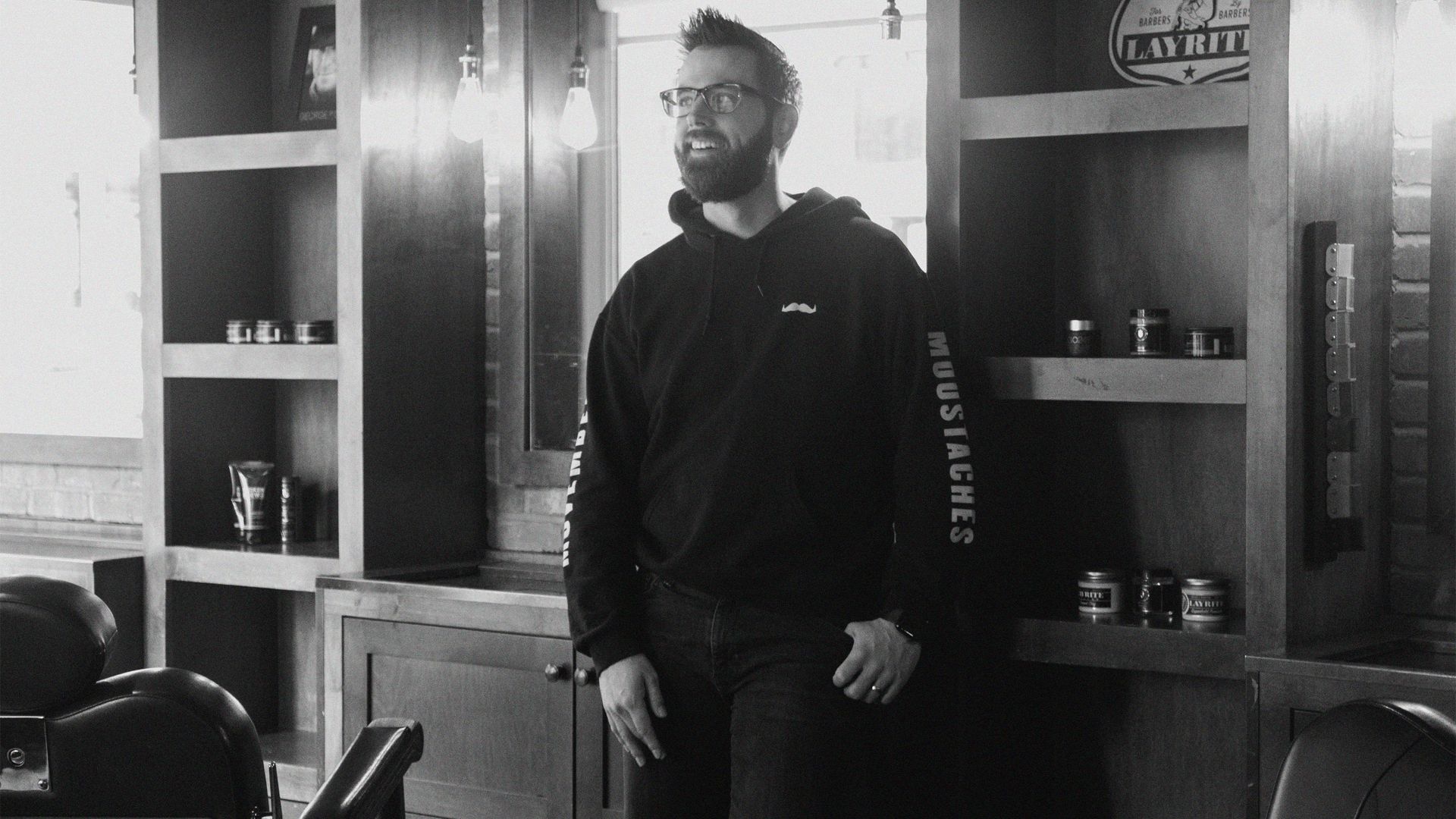 A black and white photo of a man leaning against a barbershop counter