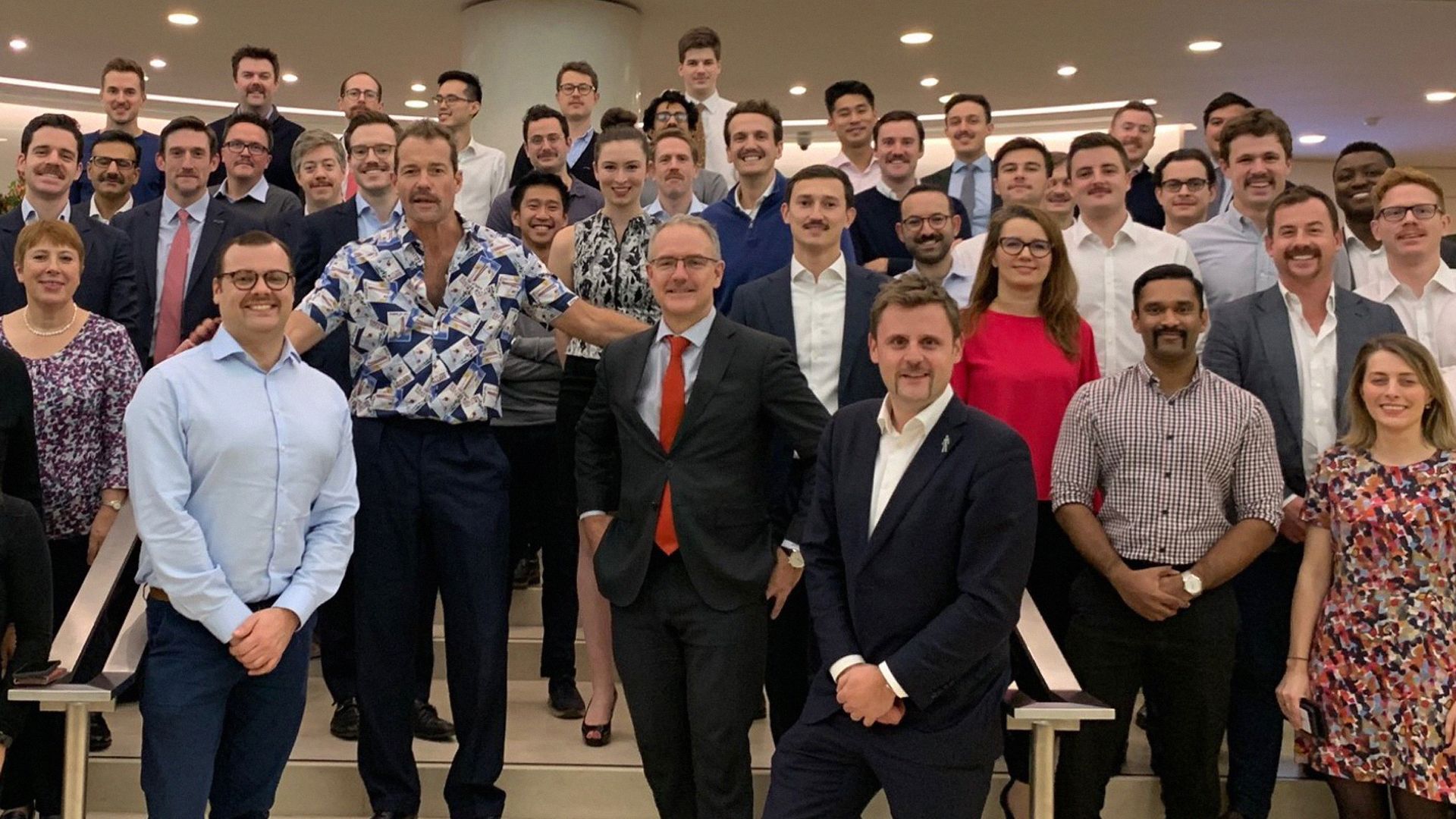 A group of colleagues pose for a Movember team photo, with most of the men sporting a moustache