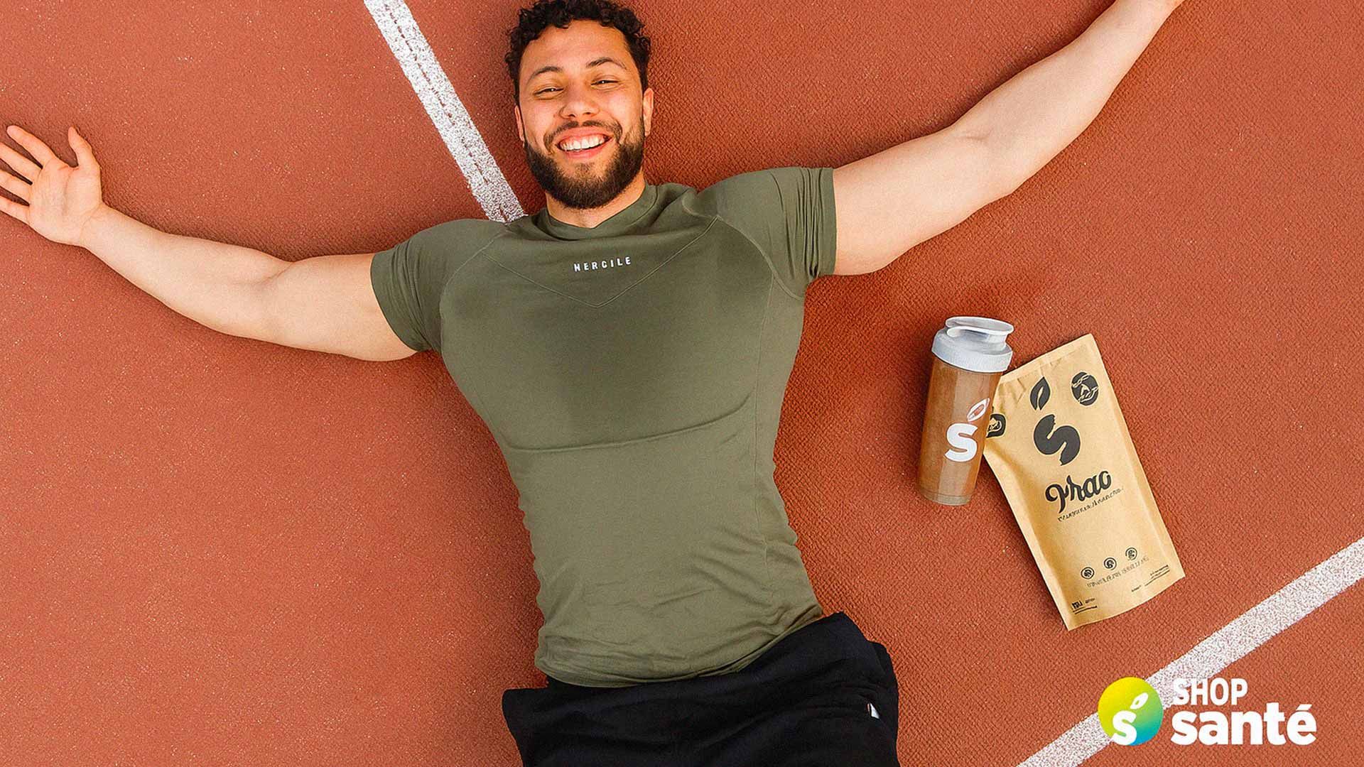 Photo of a man lying ecstatically on an athletics running track. Several Shop Santé products are beside him.