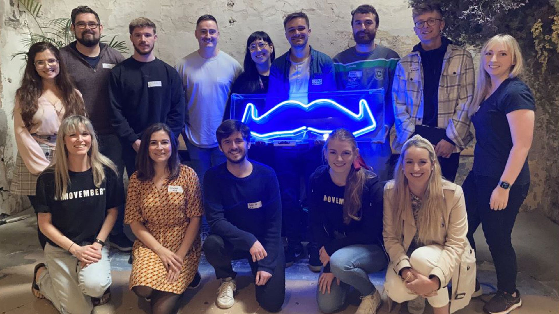 An image of a group of workplace employees supporting Movember with a neon moustache light.