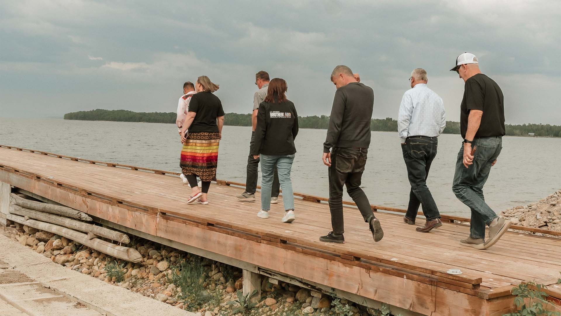 Sombre image of seven people walking in a peer, looking out to sea.