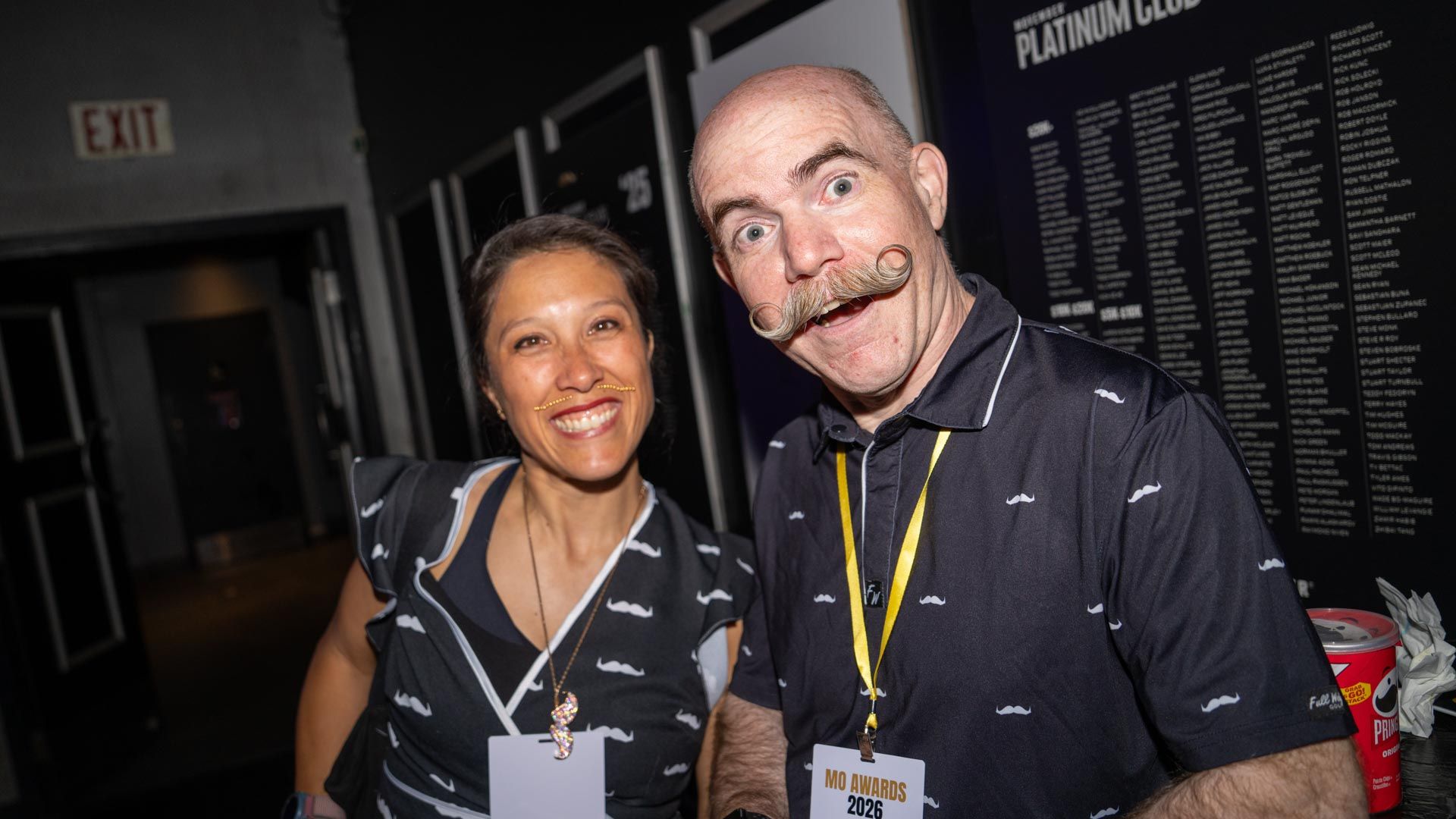 Two people with moustaches and moustache merch tops