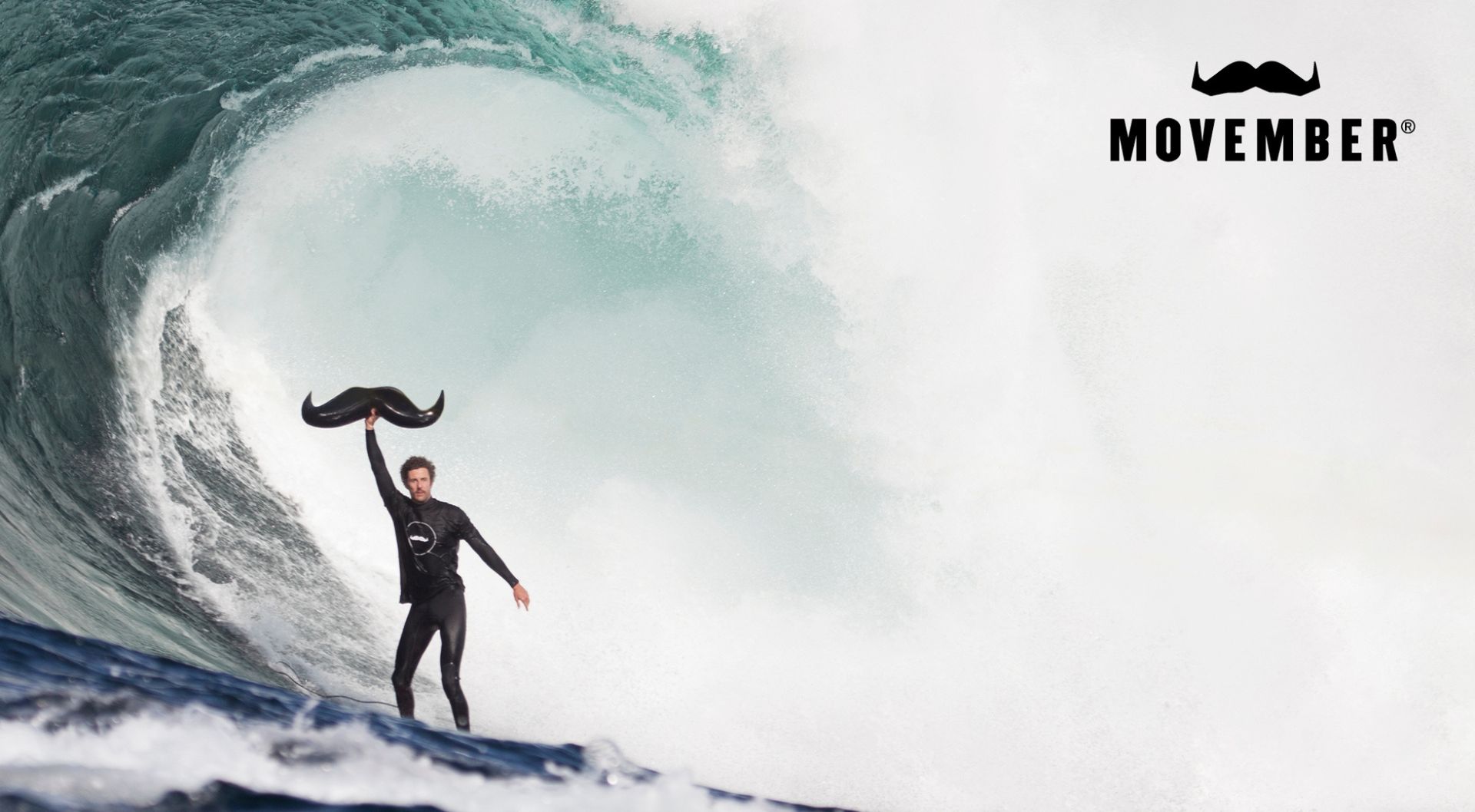 Man surfing a big wave holding an inflatable moustache above his head