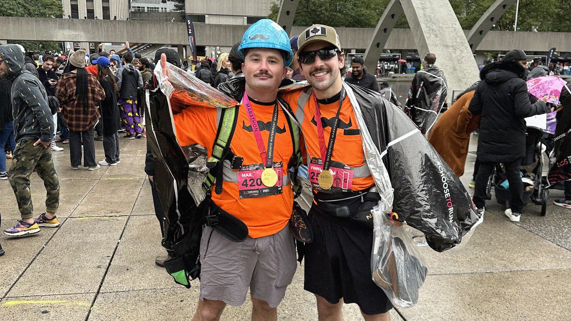 Two moustachioed men wearing construction gear pose at the end of a marathon run they've just completed in Toronto