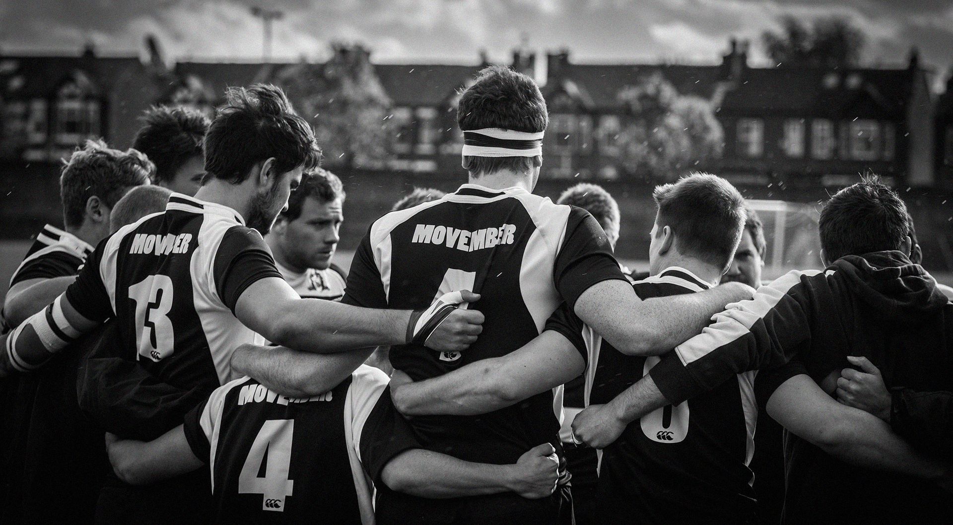 A group of young men in sports jerseys embrace in between plays on a field