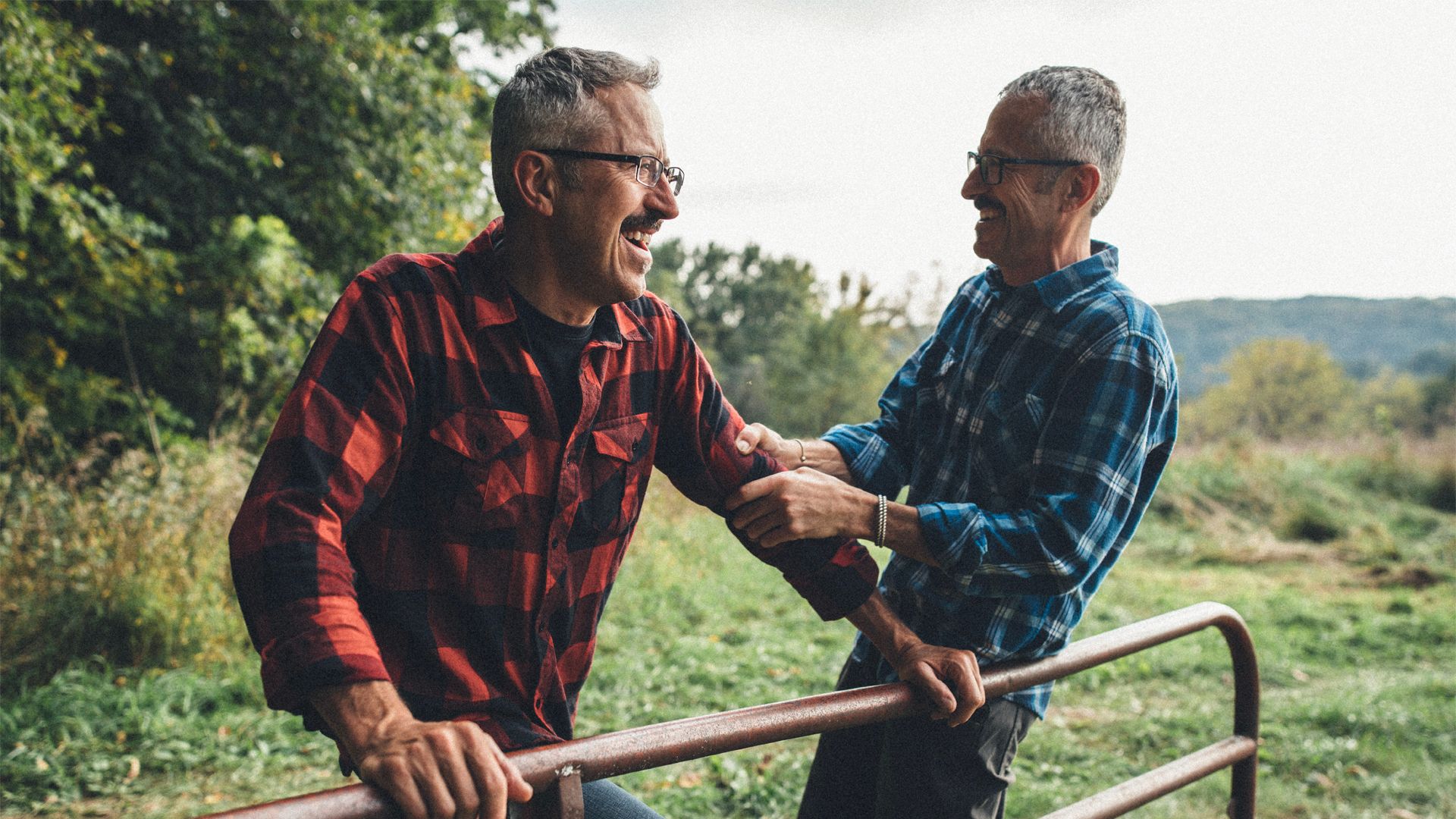 Twin brothers laughing with one another in a rural setting.