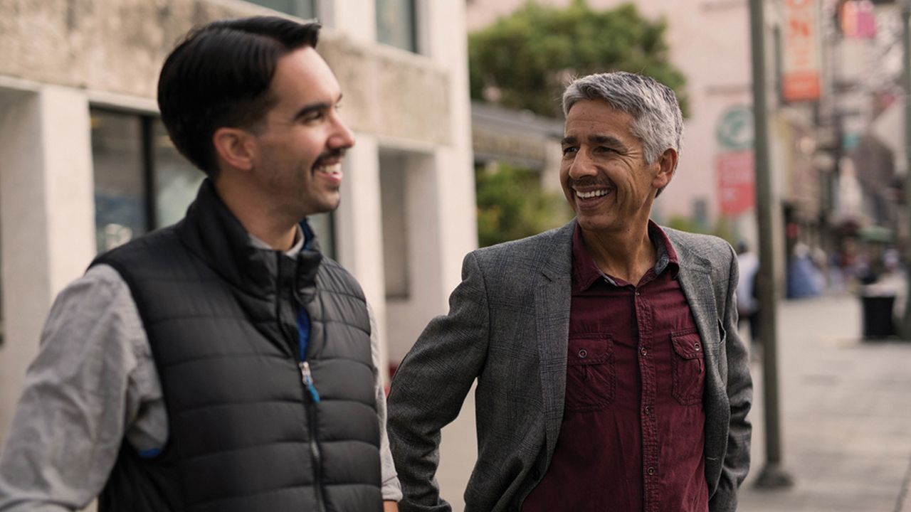 Photo of two smiling men having a conversation on the street.