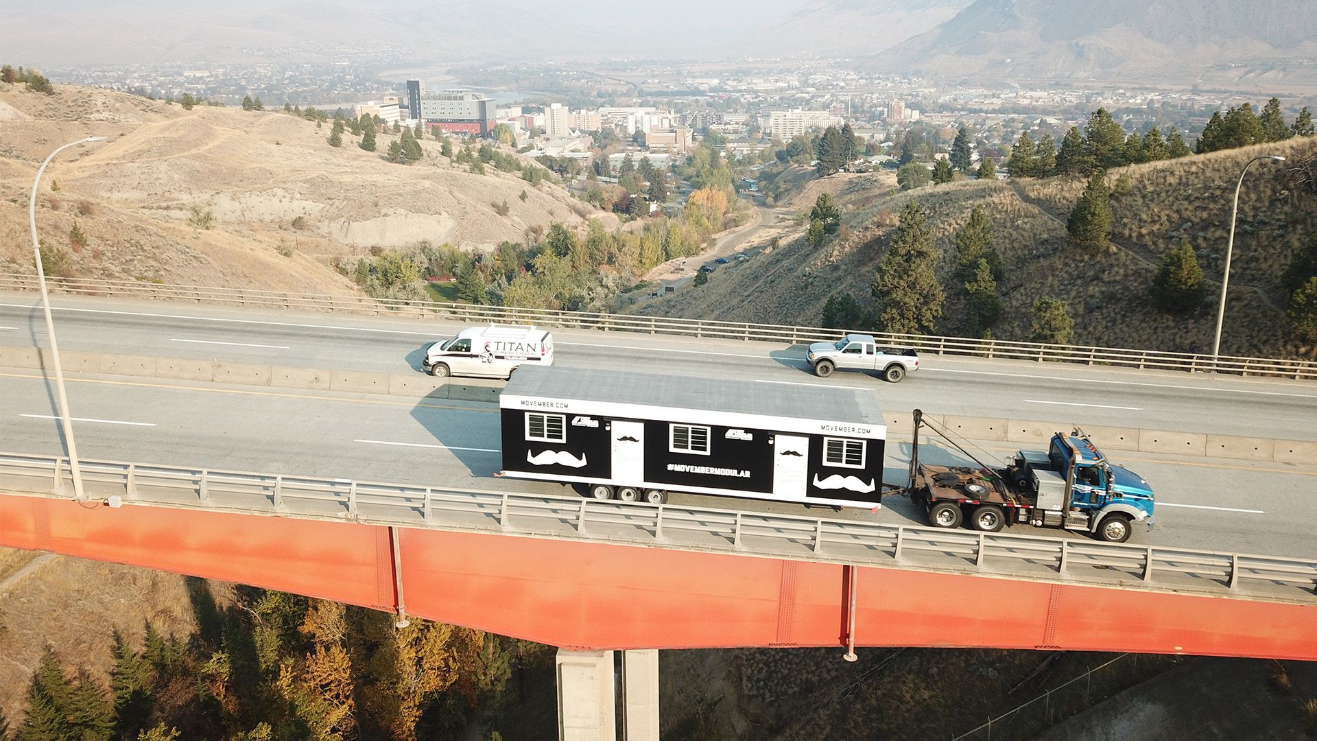 A truck pulls a construction trailer with Movember branding on it.