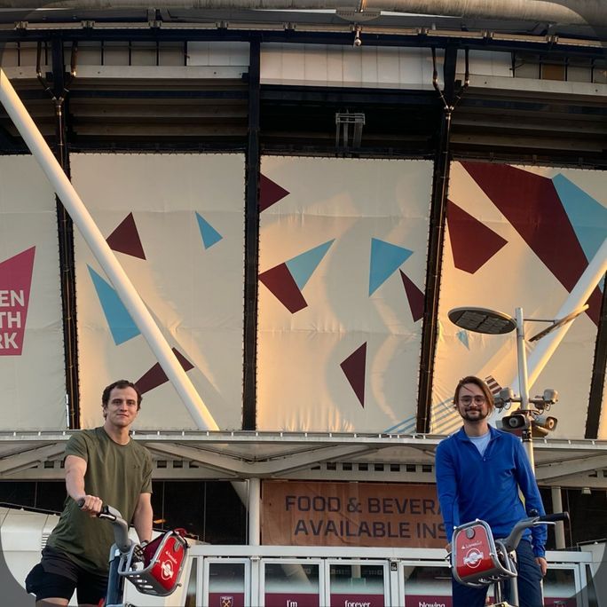 Photo of two young men, riding push-bikes, looking to camera.