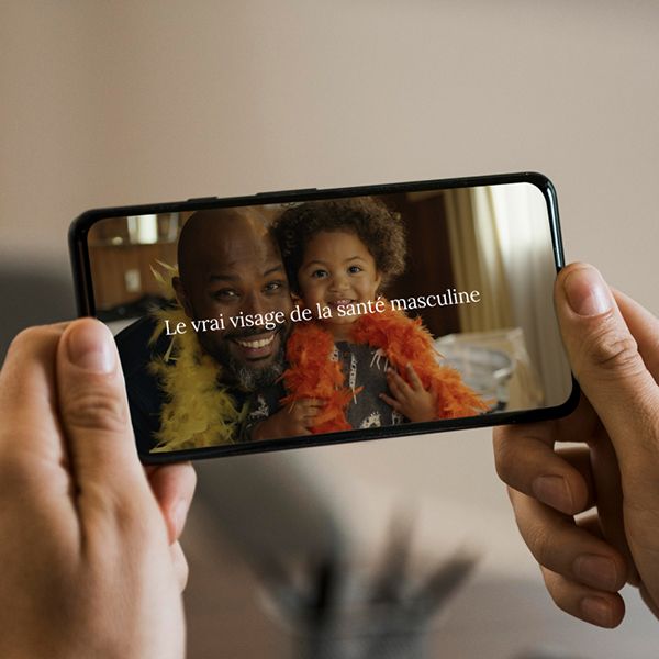 Photo of a phone, playing a video about the Real Face of Men's Health, with French text superimposed.