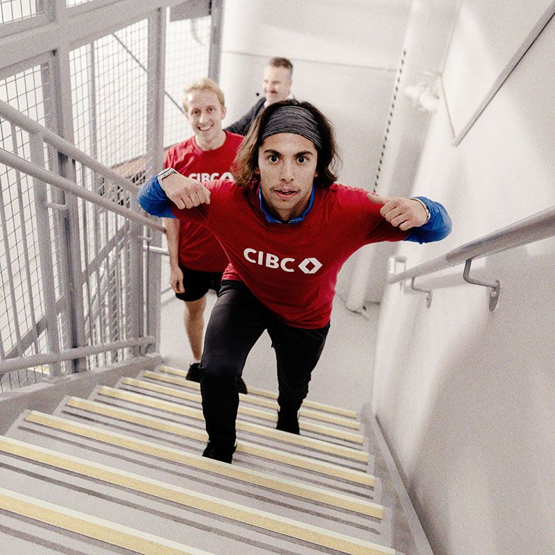 Photo of a young man enthusiastically climbing stairs, wearing a CIBC-branded shirt.