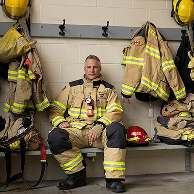 Photo of firefighter in full working gear, seated in a station change room.