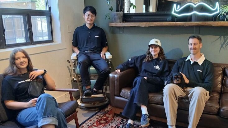Photo showing four seated people wearing Movember-branded merchandise.