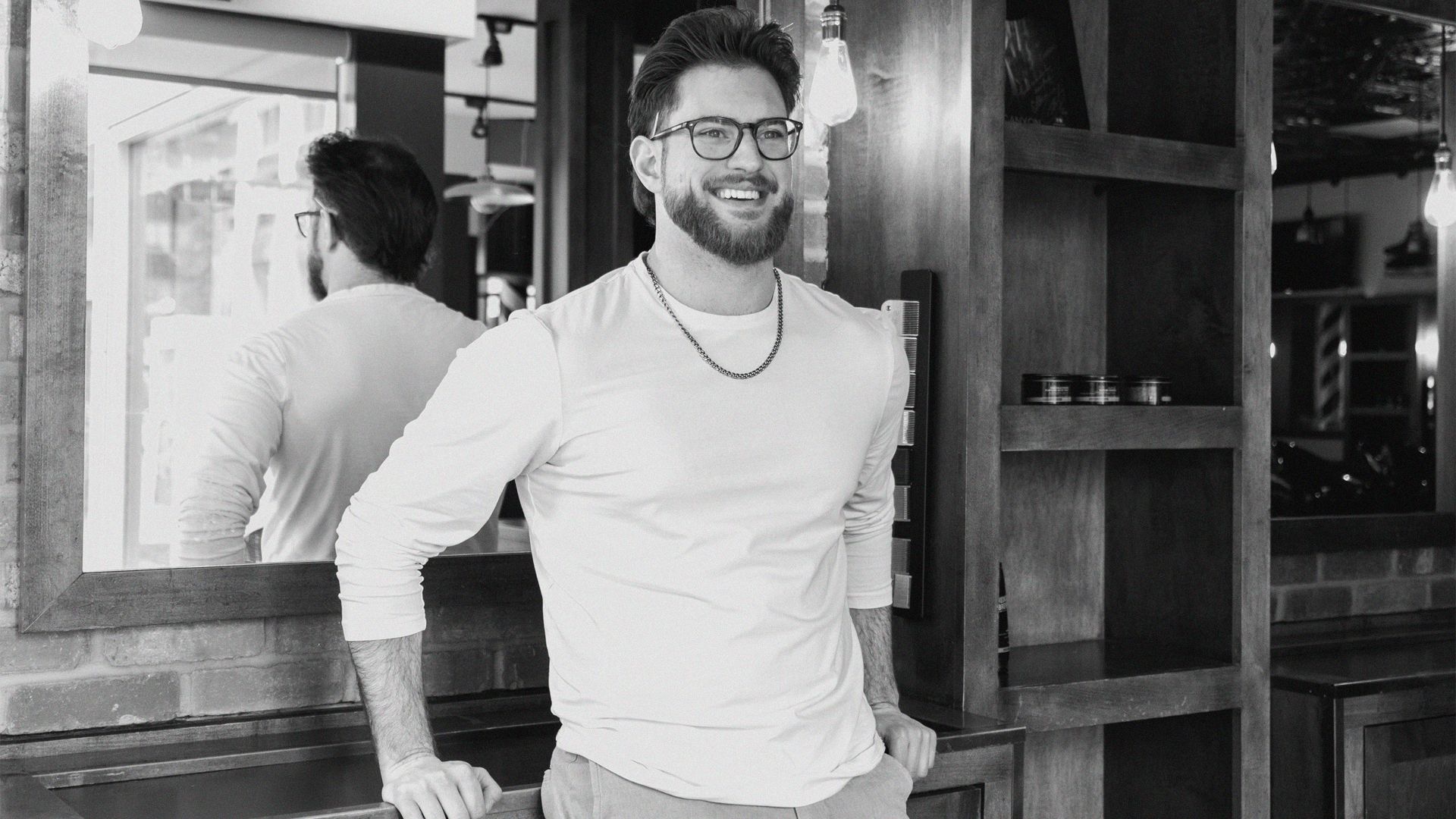 A black and white photo of a man leaning up against a barbershop counter