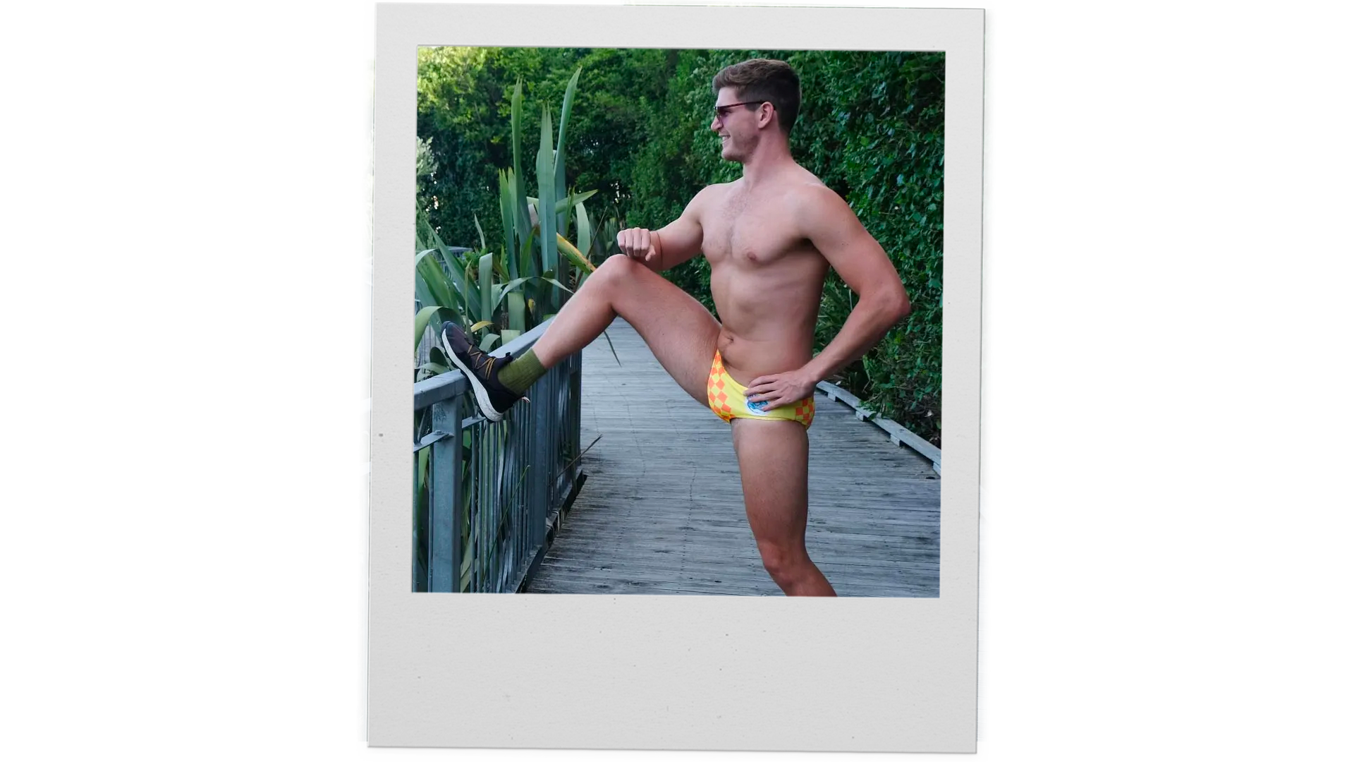 A polaroid photo of a man in Speedo's stretching before a run.