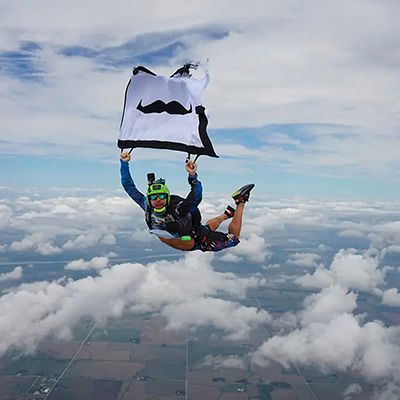 Photo of a skydiver in mid-dive, holding a Movember-branded flag.