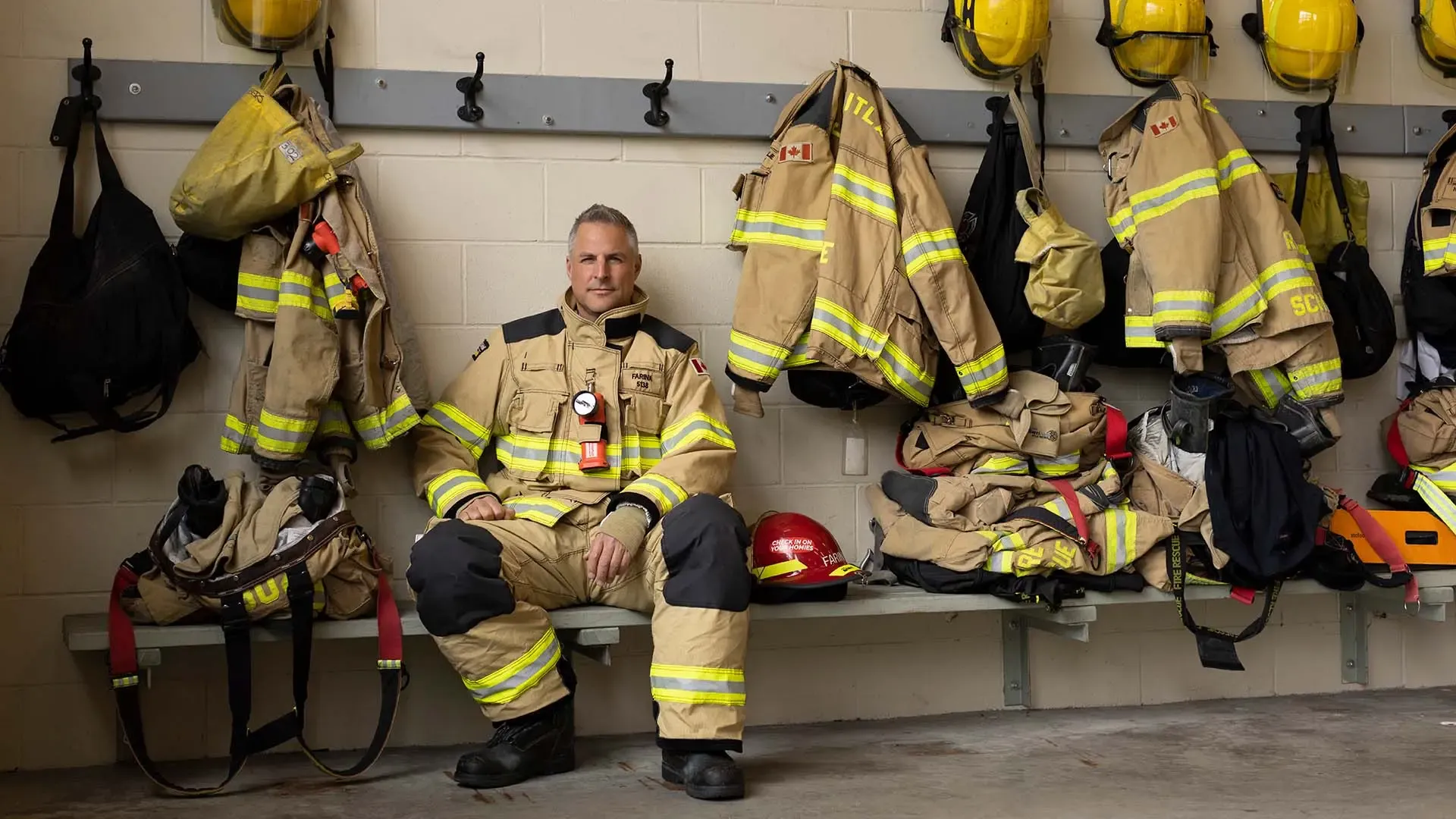 Firefighter in full gear, sitting in station's change room, looking to camera.