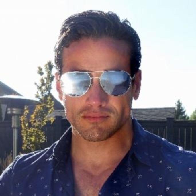 Portrait photo of man sporting gleaming sunglasses, looking determinedly to camera.