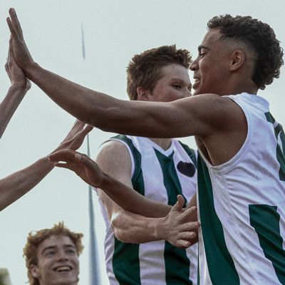 Teenage footballers in uniform high-fiving each other on a football oval.