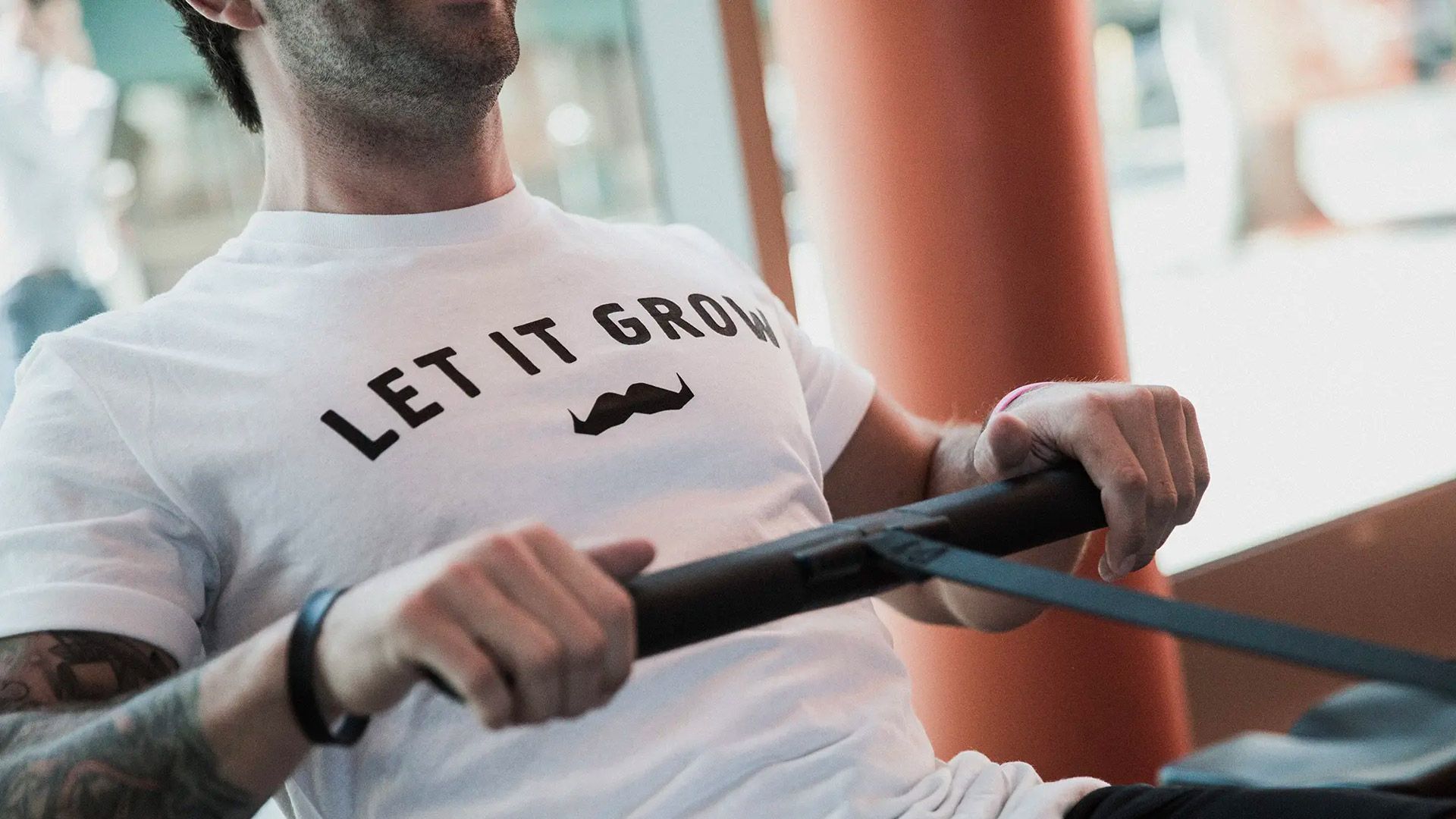 Photo of a man on a rowing machine wearing a t-shirt with the Movember logo and text which says "Let it grow"