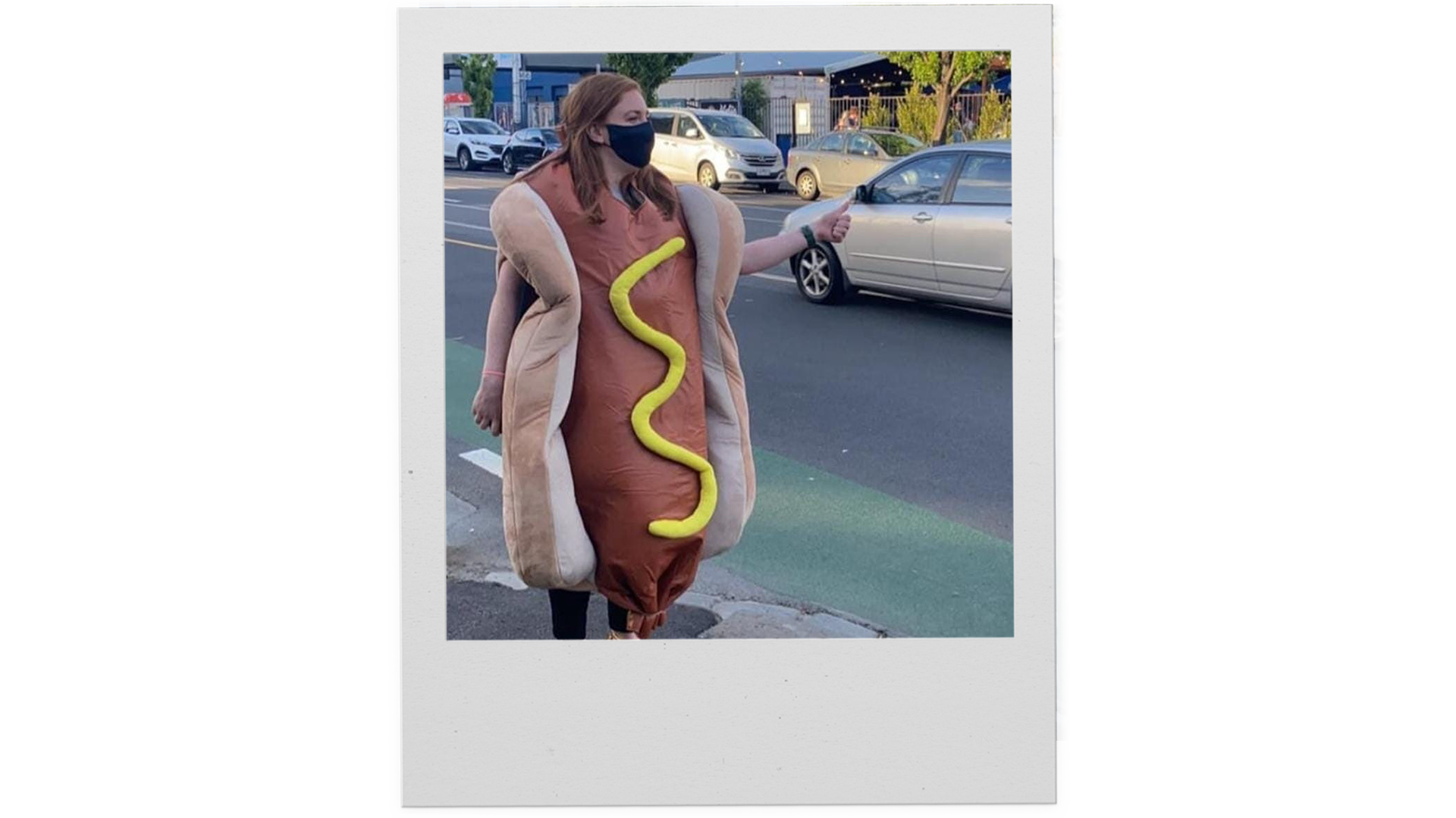 A polaroid photo of a woman in a hot dog costume hitch-hiking.