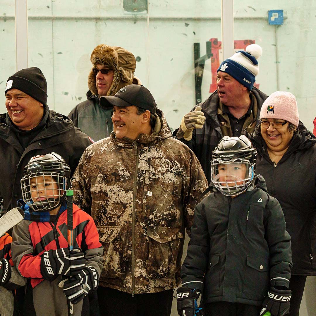 Photo of a smiling group of people watching an ice hockey game from the sidelines.