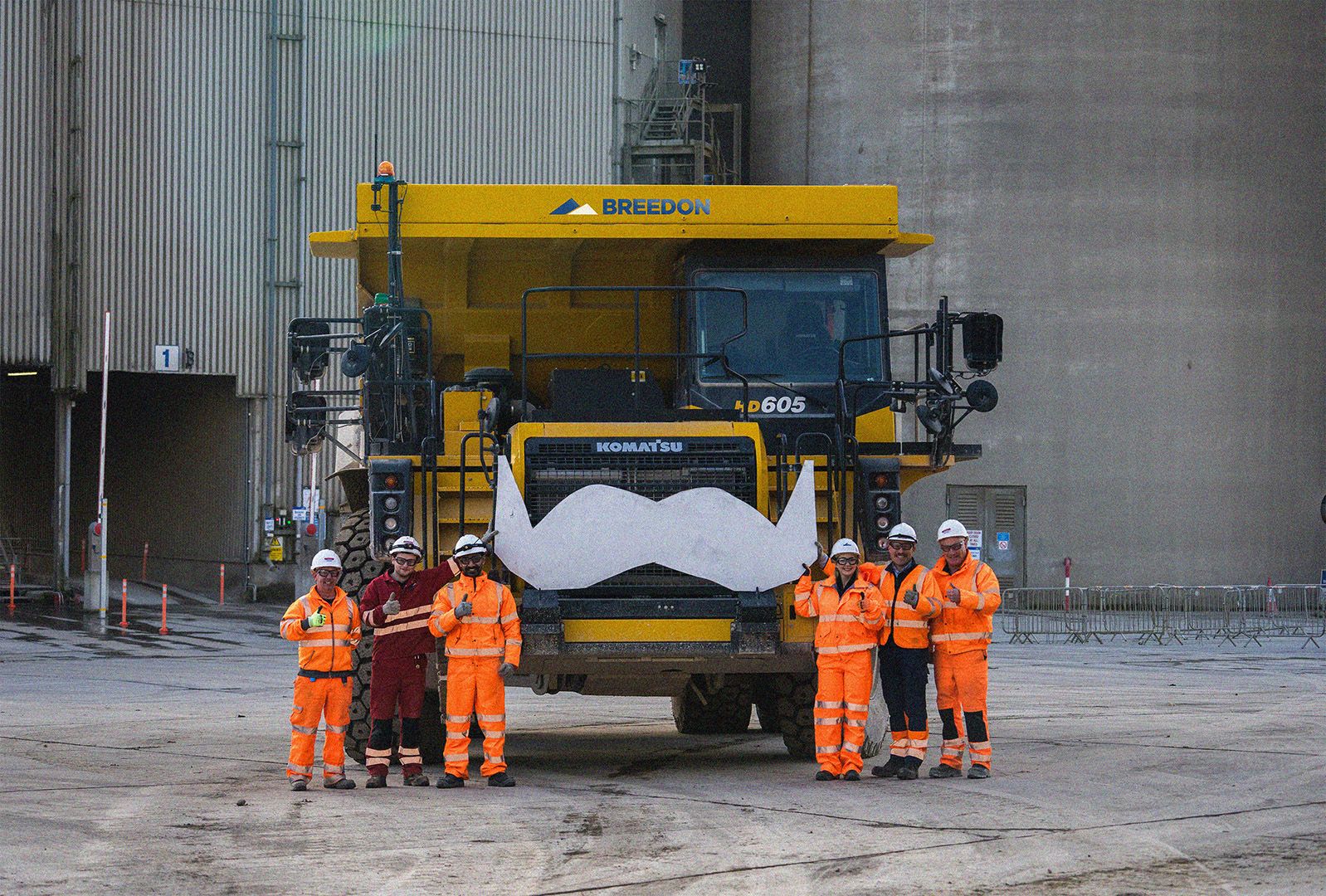 A group of construction workers smile and pose in front of a large piece of machinery.