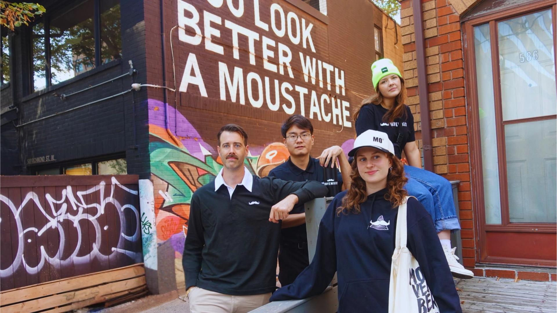 Photo showing four seated people wearing Movember-branded merchandise.