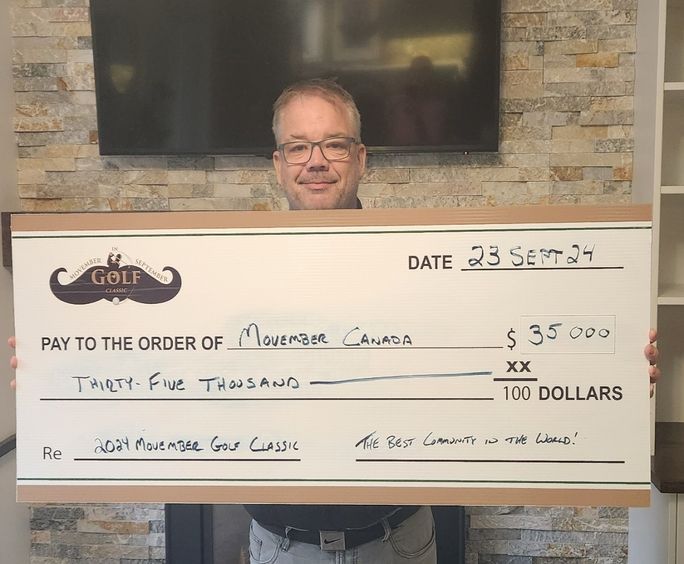 Photo of a man holding up a signed oversize novelty cheque, destined for Movember Canada.