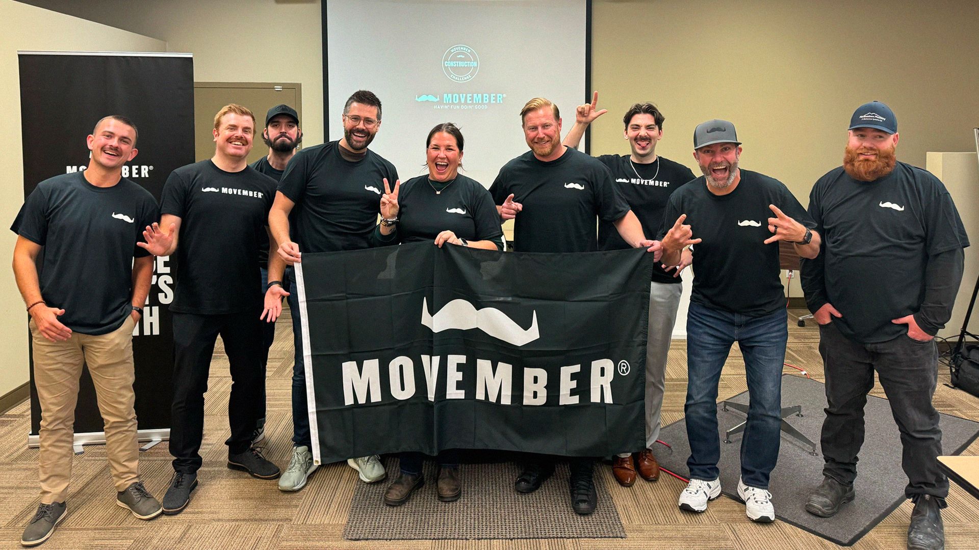 Group of men hold a flag with Movember logo